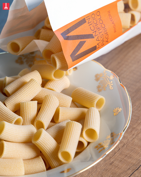 Pasta being poured from a branded package into a decorative bowl.